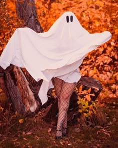 a woman dressed as a ghost sitting on a tree stump in front of some leaves