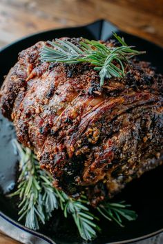 a large piece of meat sitting on top of a pan covered in rosemary sprigs