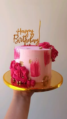 a hand holding a pink and gold birthday cake