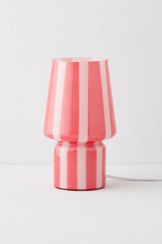 a pink and white striped lamp with a cord attached to the light bulb, on a white surface