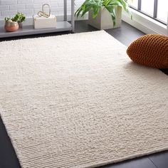 a white rug on the floor in front of a window with potted plants next to it