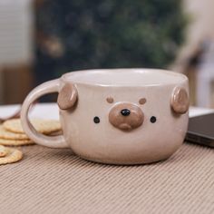 a coffee cup with a bear face on it next to crackers and a cell phone