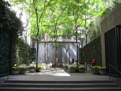 people are sitting at tables in the middle of a courtyard with trees and bushes on either side