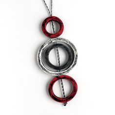 two circular pendants hanging from a chain on a white surface with red and black rings