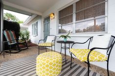 two chairs and a table on the front porch with yellow patterned cushions, one chair has a footstool