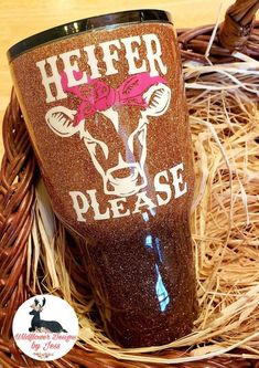 a cup that is sitting on some straw in a basket with the words heifer please painted on it