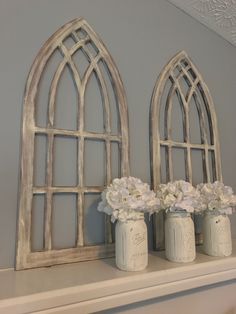 two white vases with flowers are sitting on a mantle next to an old window