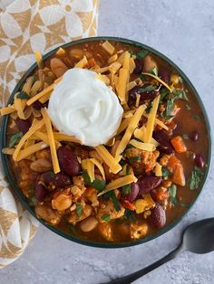 a bowl filled with chili and beans topped with sour cream on top of a table