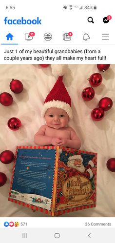 a baby wearing a santa hat and holding a christmas book with red ornaments around it