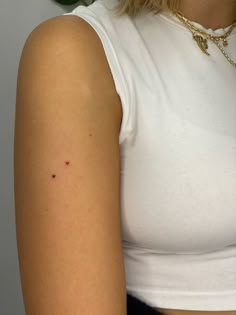 a close up of a person wearing a white tank top and gold necklace with small black dots on her arm