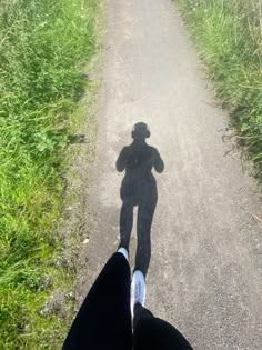 a person standing in the middle of a dirt road with their shadow on the ground