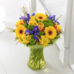 a vase filled with yellow and blue flowers on top of a white table next to a mirror