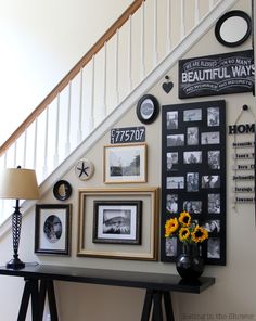 a wall with pictures, frames and flowers on it next to a stair case in a home