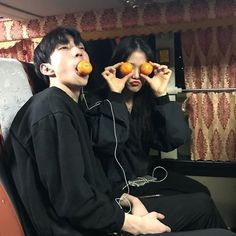 two people sitting on a train with oranges in their mouths