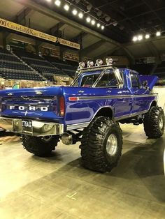 a large blue truck with big tires on display in a showroom at an indoor event