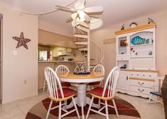 a dining room table with four chairs and a spiral stair case in the back ground