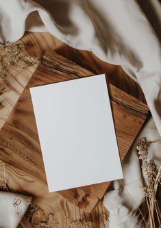 an empty white card sitting on top of a wooden table next to some dried flowers