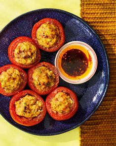 an overhead view of some stuffed red peppers on a blue plate with a small bowl of ketchup