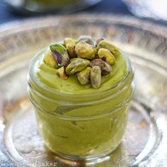 a glass plate topped with a jar filled with green liquid and pistachios