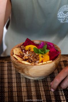 a person sitting at a table with a wooden bowl filled with food on top of it