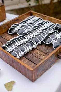 a wooden box filled with sunglasses on top of a white table cloth covered tablecloth