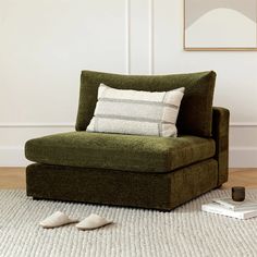 a green chair with two pillows on top of it next to a pair of slippers