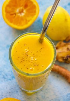 a glass filled with orange juice next to sliced lemons and ginger on a blue surface