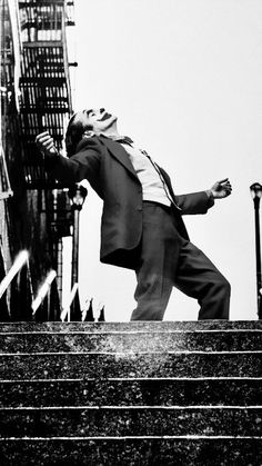 a black and white photo of a man in a suit climbing up some stairs with his arms outstretched