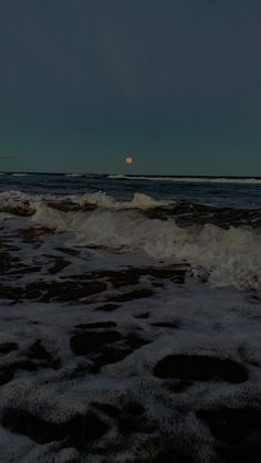 the moon is setting over the ocean waves