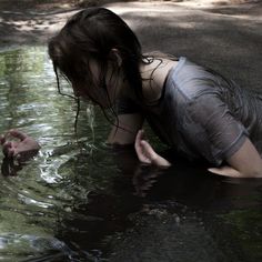 a woman is in the water with her hand out and looking at something on the ground