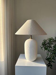 a white lamp sitting on top of a table next to a potted green plant