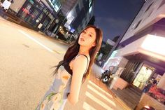 a woman standing in the middle of a street at night with her arms behind her back