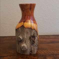 a wooden vase sitting on top of a table next to a white wall and wood floor