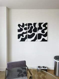 two black and white paintings hang on the wall above a glass table in a modern living room