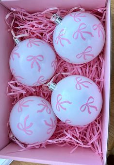 three ornaments in a pink box with ribbon on them are sitting next to each other