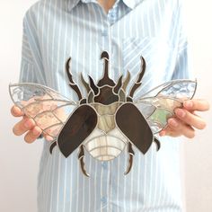 a person wearing a blue striped shirt holding a metal insect brooch in their hands