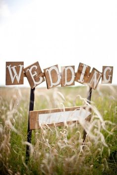 a wooden sign sitting in the middle of a grass field with words spelling wedding on it