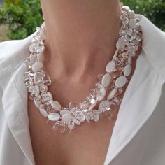 a woman wearing a white shirt and some necklaces on her neck with flowers in the background