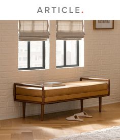 a wooden bench in front of two windows with roman shades on the window sill