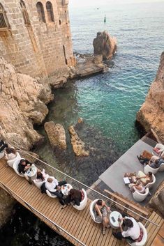 people are sitting at tables on the edge of a cliff overlooking the water and cliffs