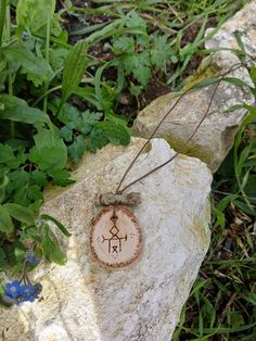 a wooden pendant with an ancient symbol on it sitting on a rock in the grass