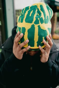 a person covering their face with a green and yellow beanie on top of his head