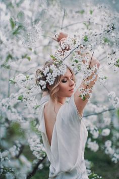 a woman in white dress holding flowers up to her head