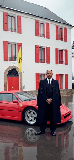 a man standing next to a red sports car in front of a white building with red shutters