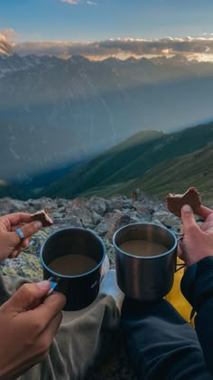 two people holding cups of coffee on top of a mountain