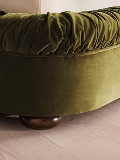 a green round bed sitting on top of a wooden floor next to a white wall