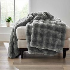 a couch with a blanket on top of it next to a potted plant and window