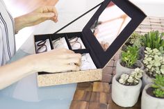 a woman is opening an open box with glasses in it on a table next to potted plants