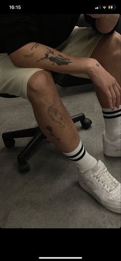 a man sitting on top of a chair with his legs crossed and tattoos on his leg