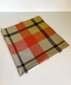 an orange, yellow and brown checkered blanket laying on top of a white table